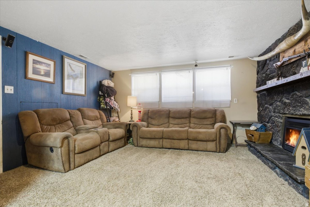 Living area featuring a stone-clad fireplace with a hearth, wall-to-wall carpeting, and multiple windows with blinds