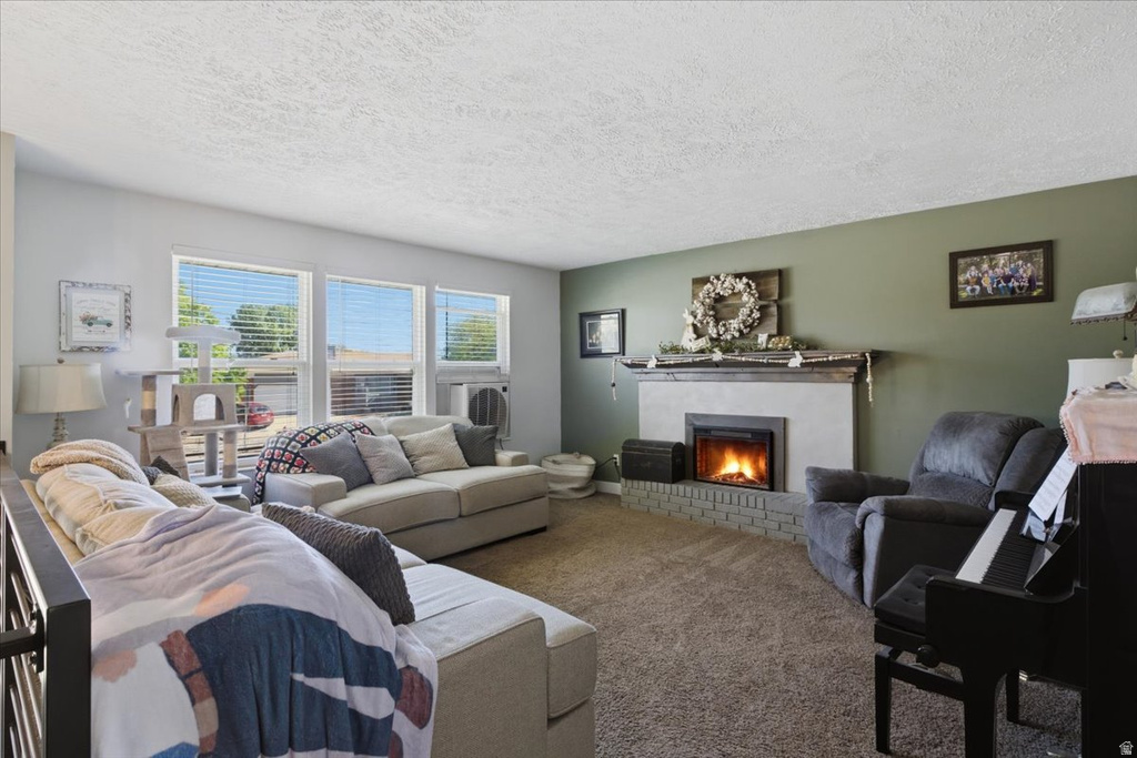 Living area featuring a white stone fireplace with a grey brick base, multiple large windows with blinds, light-toned walls, and a textured ceiling