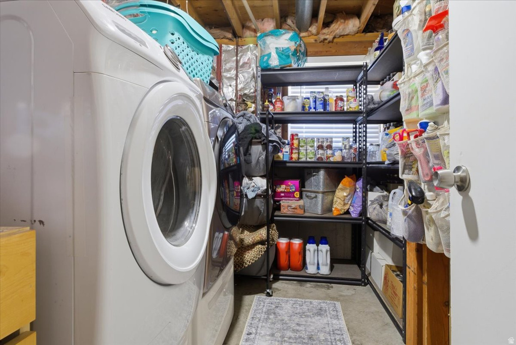 Dedicated laundry area featuring a front-load washer, utility shelving, exposed wood joists, and a concrete floor