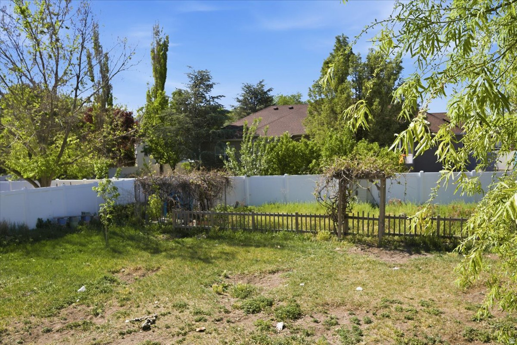 Expansive backyard featuring a white privacy fence, established green foliage, and a decorative wooden trellis