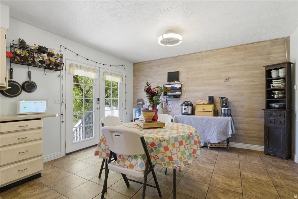 Functional dining space featuring light-colored tile flooring, a horizontal wood-finish accent wall, and double French doors opening to an outdoor area