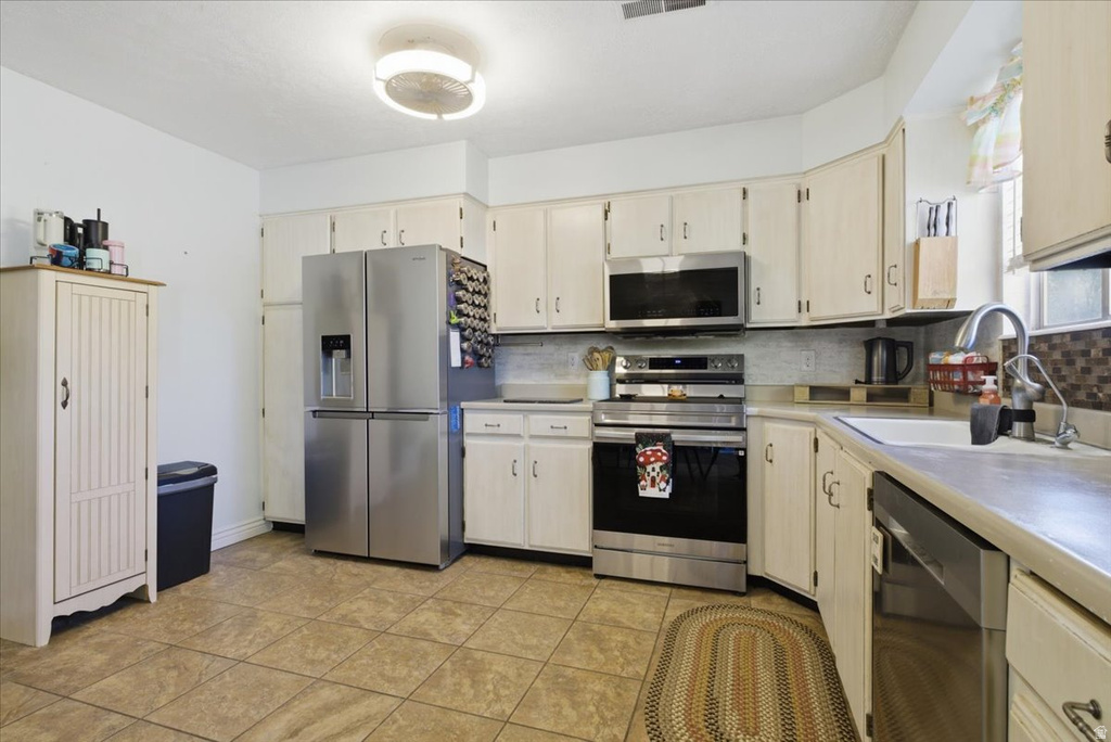 Kitchen featuring tile flooring, white cabinetry, stainless steel appliances, a tile backsplash, and a contemporary ceiling light fixture