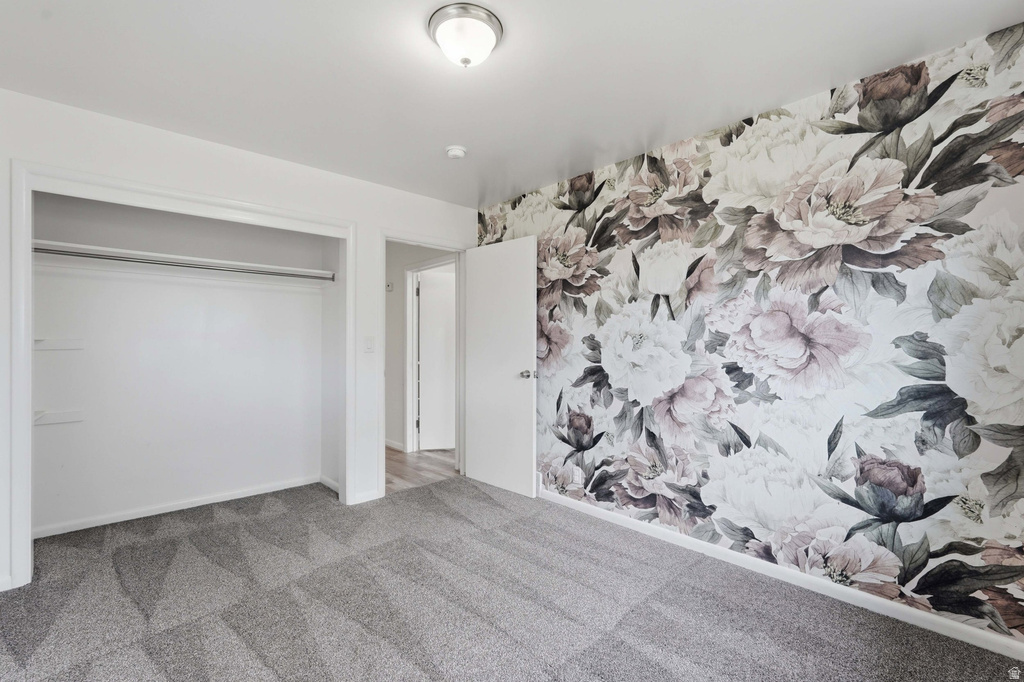 Accent wall featuring a floral pattern, neutral-toned carpeting, white trim throughout, built-in closet with shelving and hanging rod, and a flush-mount ceiling light fixture