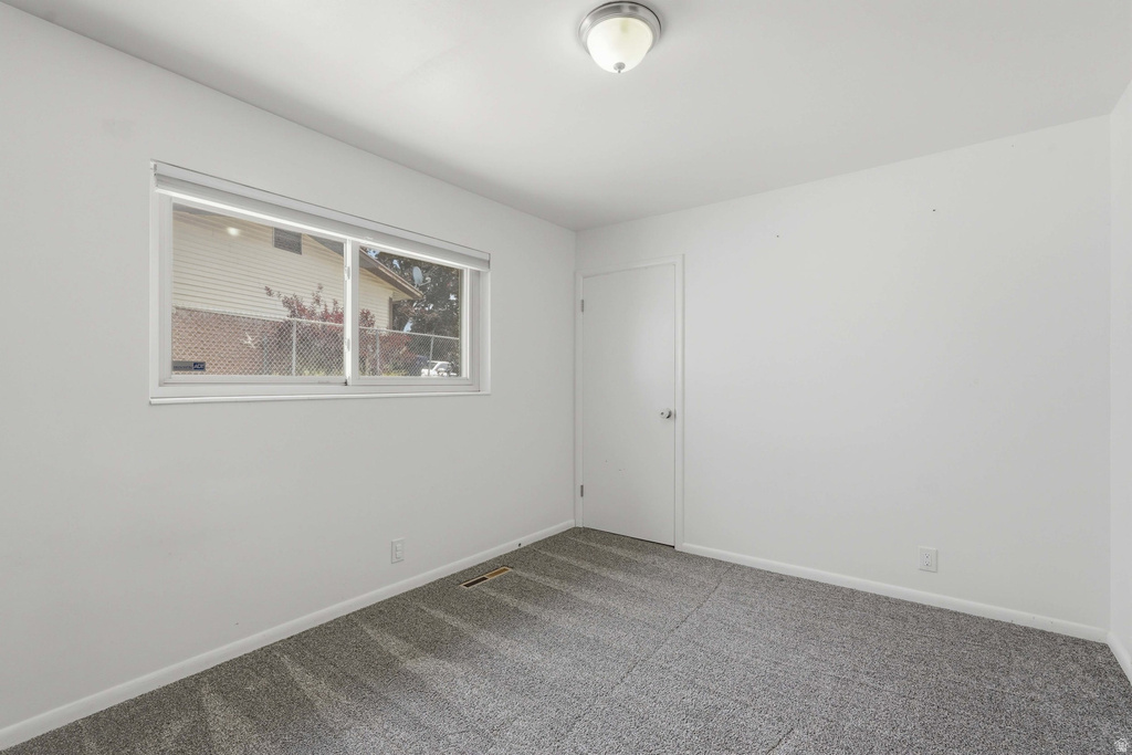 Carpeted room featuring a white interior door with a silver knob, a window with a white frame, and an overhead flush-mount light fixture