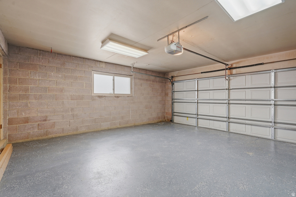 Spacious garage featuring a paneled overhead door, concrete block walls, a single window, overhead lighting, and a durable grey flooring finish
