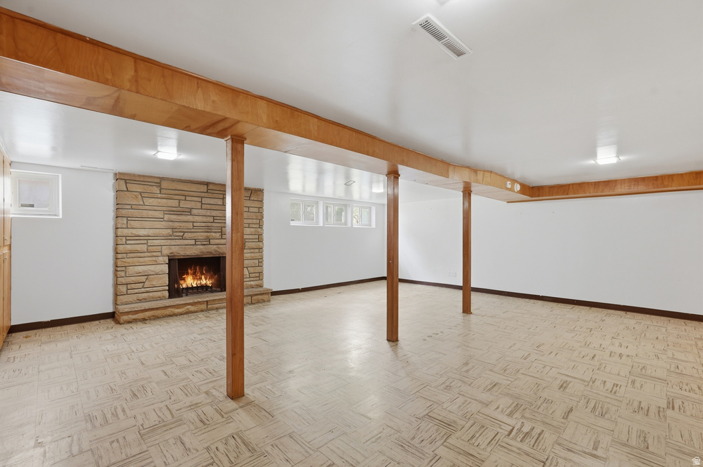 Spacious lower-level area with a stone fireplace, wood-finish columns, and ceiling beams
