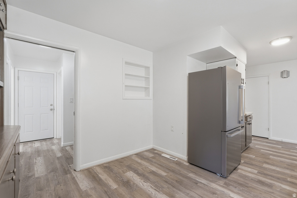 Kitchen with wood-finish flooring, recessed shelving, and a stainless steel refrigerator