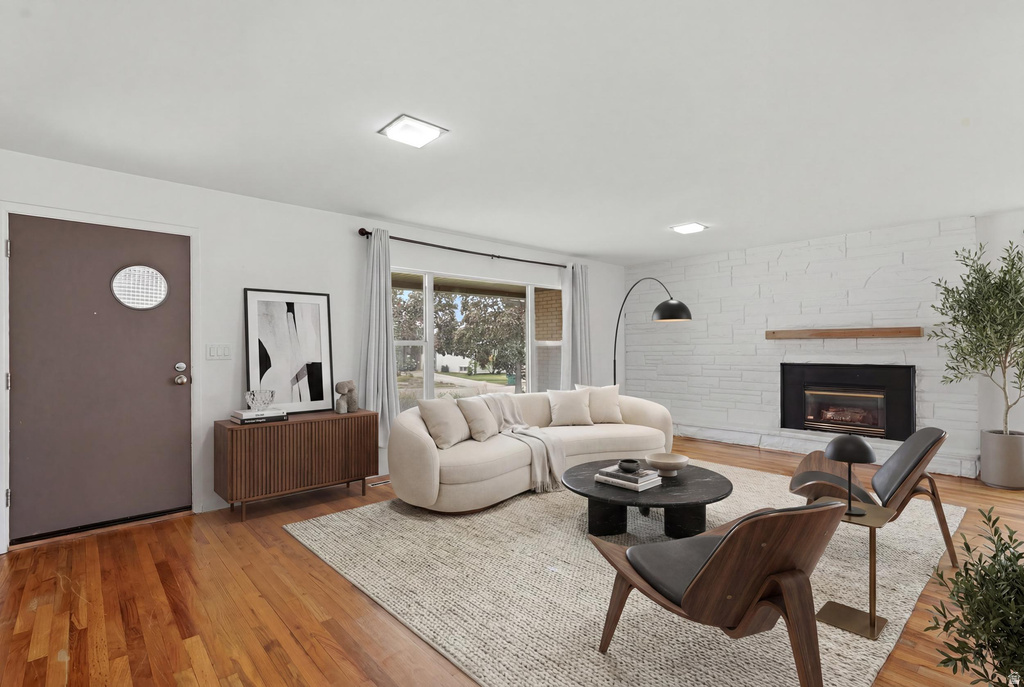 Living area featuring hardwood flooring, a white-painted brick fireplace with a wood mantle, and a front entry door with an oval window