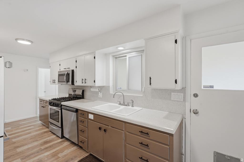 Kitchen featuring stainless steel appliances, wood-finish flooring, white upper cabinetry, brown lower cabinetry, and light countertops with a white double-basin sink
