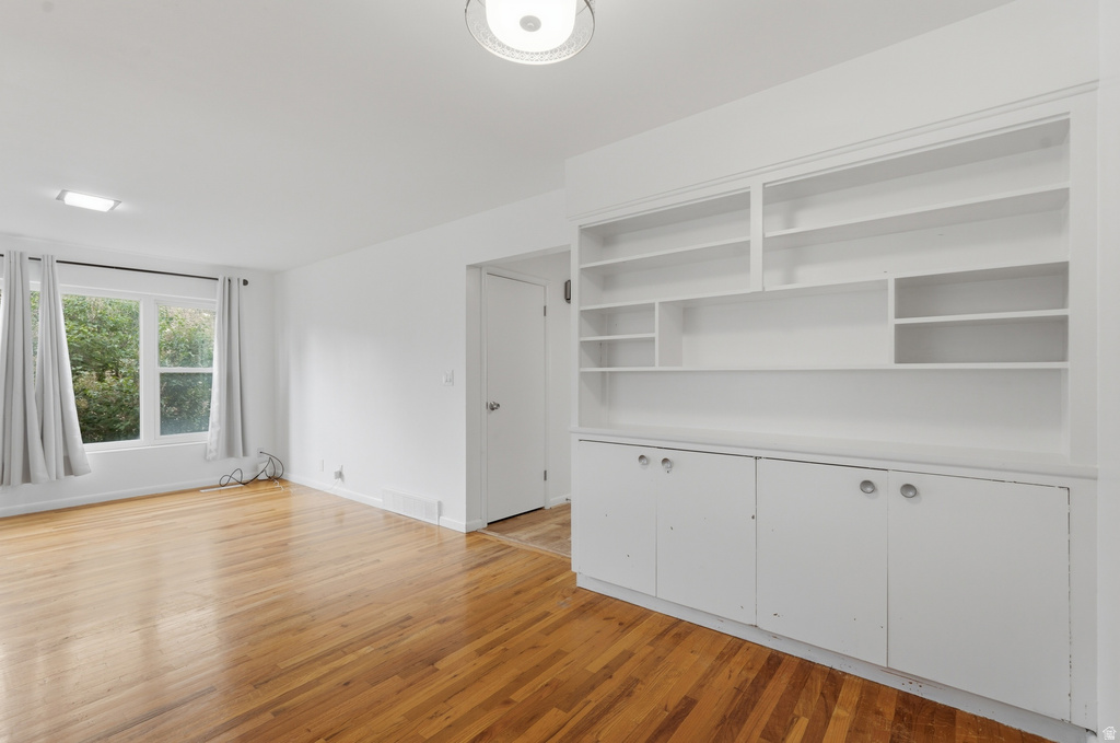 Living area featuring hardwood flooring, built-in shelving and cabinetry, recessed lighting, and a large window