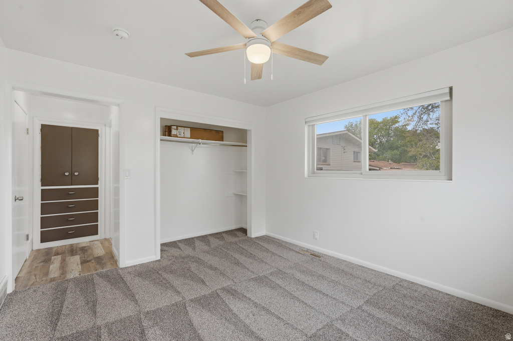 Bright room featuring a wood-finish ceiling fan, patterned gray carpet, white walls, and a window with roller shades
