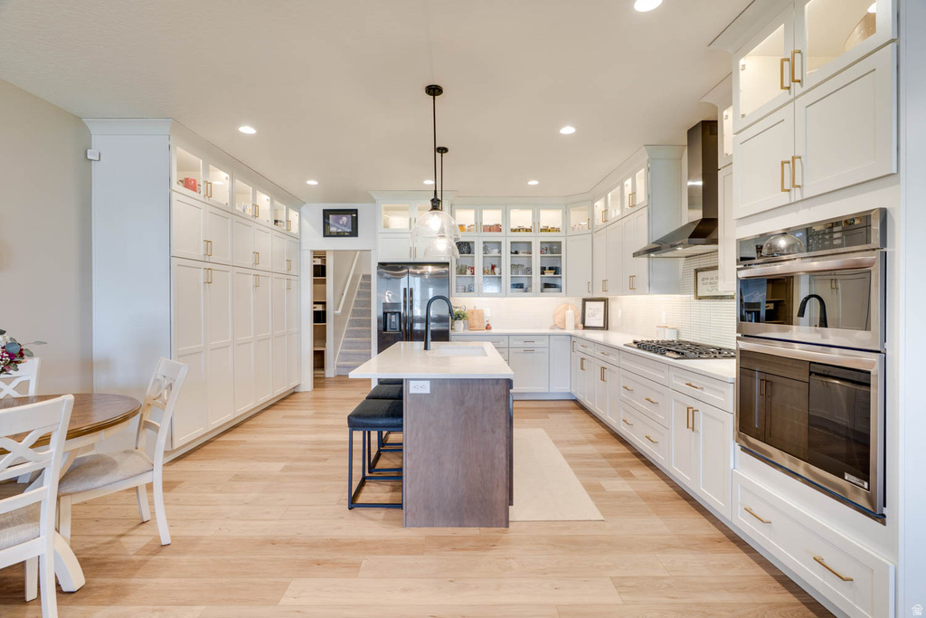 Spacious kitchen featuring an expansive island with seating, a gas cooktop, built-in double ovens, extensive white cabinetry, and wood-finish flooring