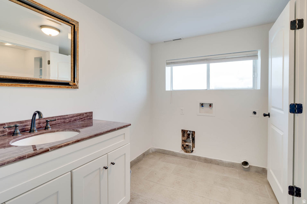 Utility space featuring a vanity with a reddish-brown countertop, an oval undermount sink, and a dark bronze faucet