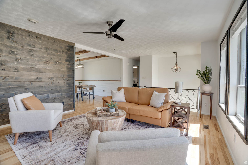 Living area featuring a prominent wood-panel accent wall, light wood-finish flooring, a ceiling fan, and multiple windows