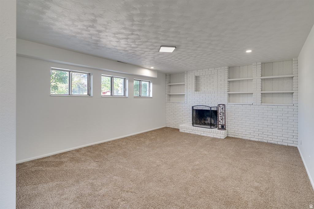Spacious room featuring a white brick fireplace with a black metal screen, built-in shelving, three windows, and carpet flooring