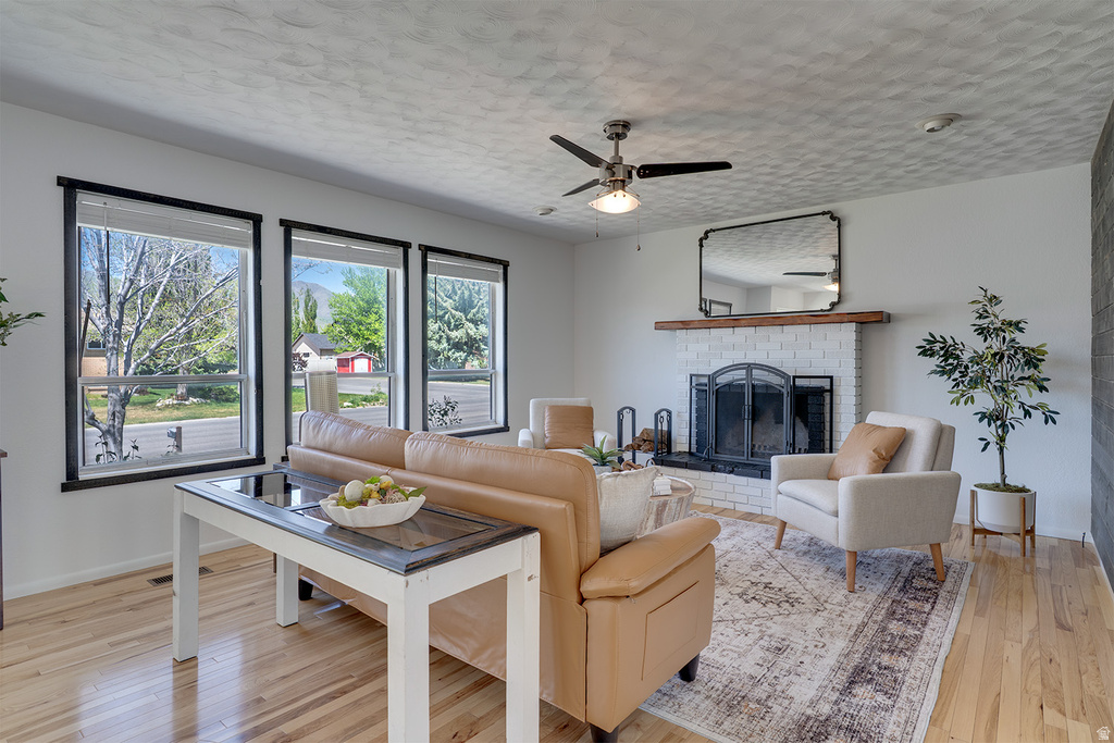 Bright living area featuring wood-finish flooring, a white brick fireplace with a wood mantle, and a ceiling fan