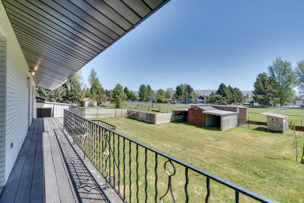 Upper-level outdoor deck featuring wood-finish flooring, a black wrought iron railing, and a sloped soffit