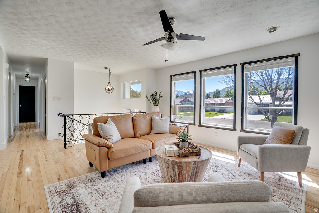 Bright living area featuring light wood-finish flooring, a decorative wrought iron railing, and a black ceiling fan with an integrated light kit