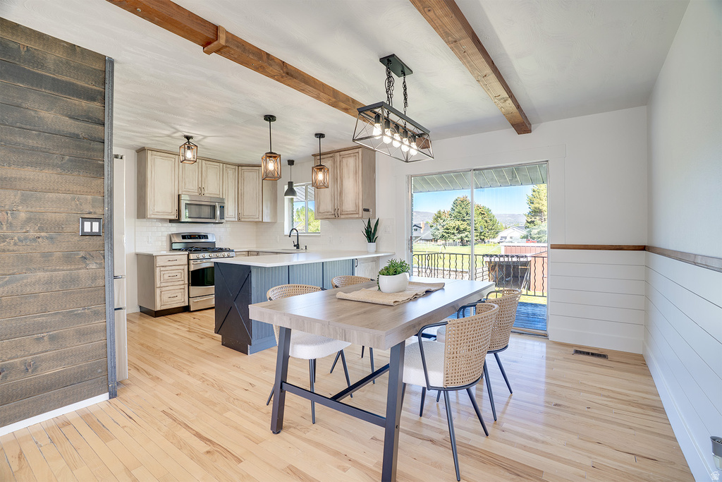 Open-concept kitchen and dining area featuring light wood-finish flooring, a kitchen island with seating, exposed wood ceiling beams, white shiplap wall accents, and sliding glass door access to an outdoor space