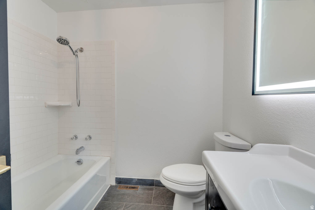 Bathroom featuring a white subway tile shower surround, a white bathtub with a chrome showerhead, a white toilet, and a white integrated sink countertop