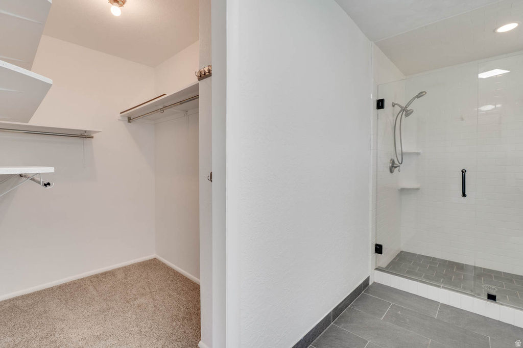 Walk-in closet with carpet flooring and shelving, paired with a shower featuring a glass enclosure, subway tile surround, and dark-toned floor tile