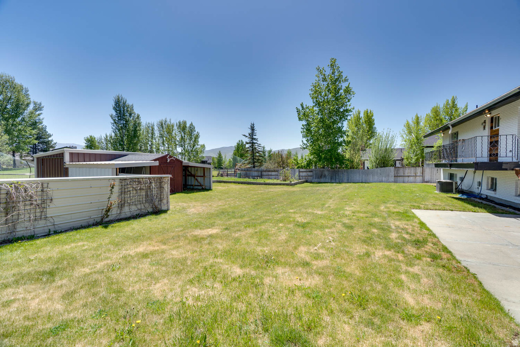 Expansive rear yard featuring green grass, a wooden fence, and mature trees