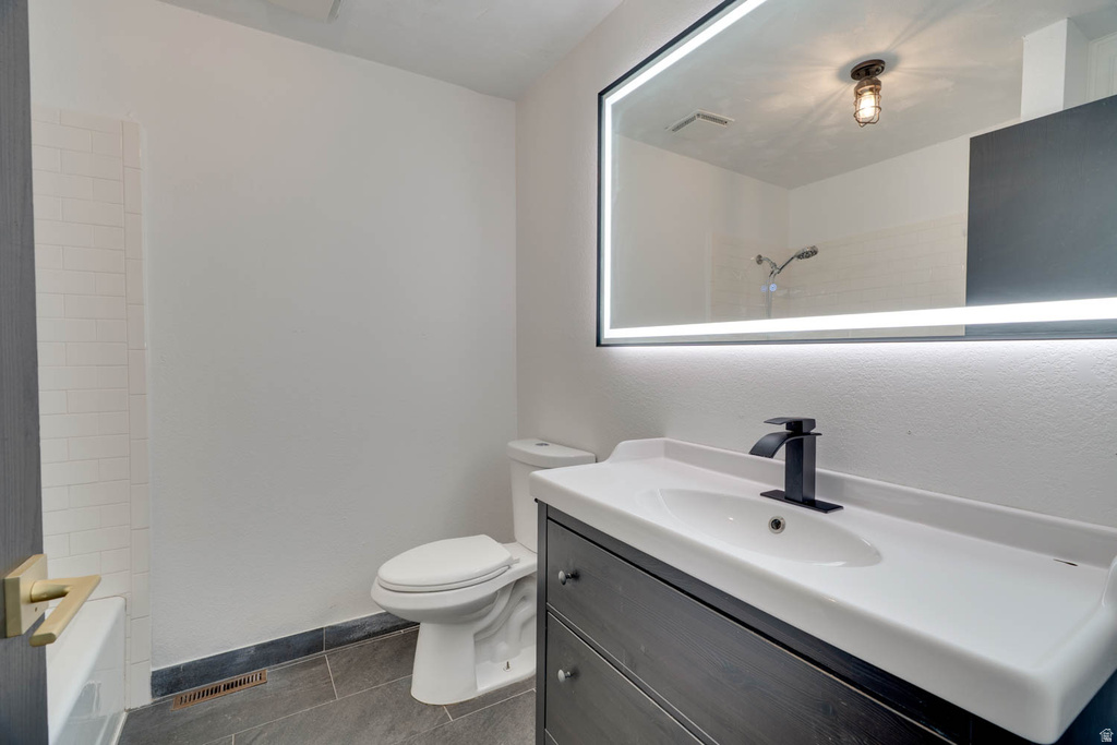 Bathroom featuring a dark wood-finish vanity with a white integrated sink, matte black waterfall faucet, and an illuminated rectangular mirror