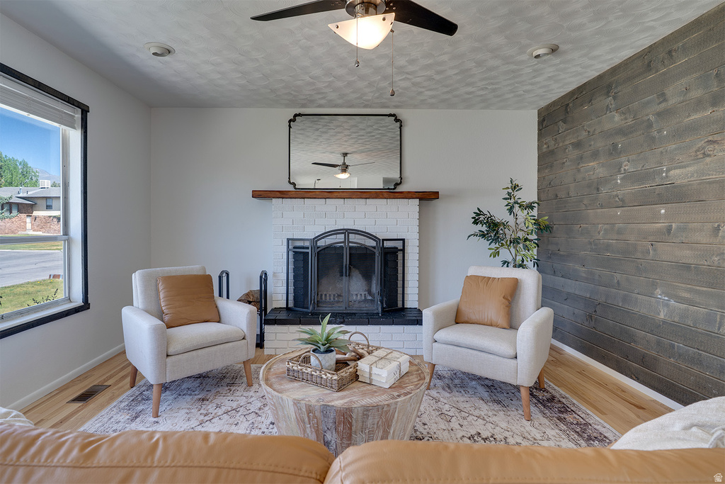 Living area featuring a white brick fireplace with a wood mantle, an overhead ceiling fan, and wood-finish flooring