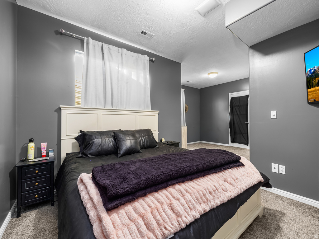 Carpeted sleeping area featuring a cream-colored paneled headboard and dark gray walls