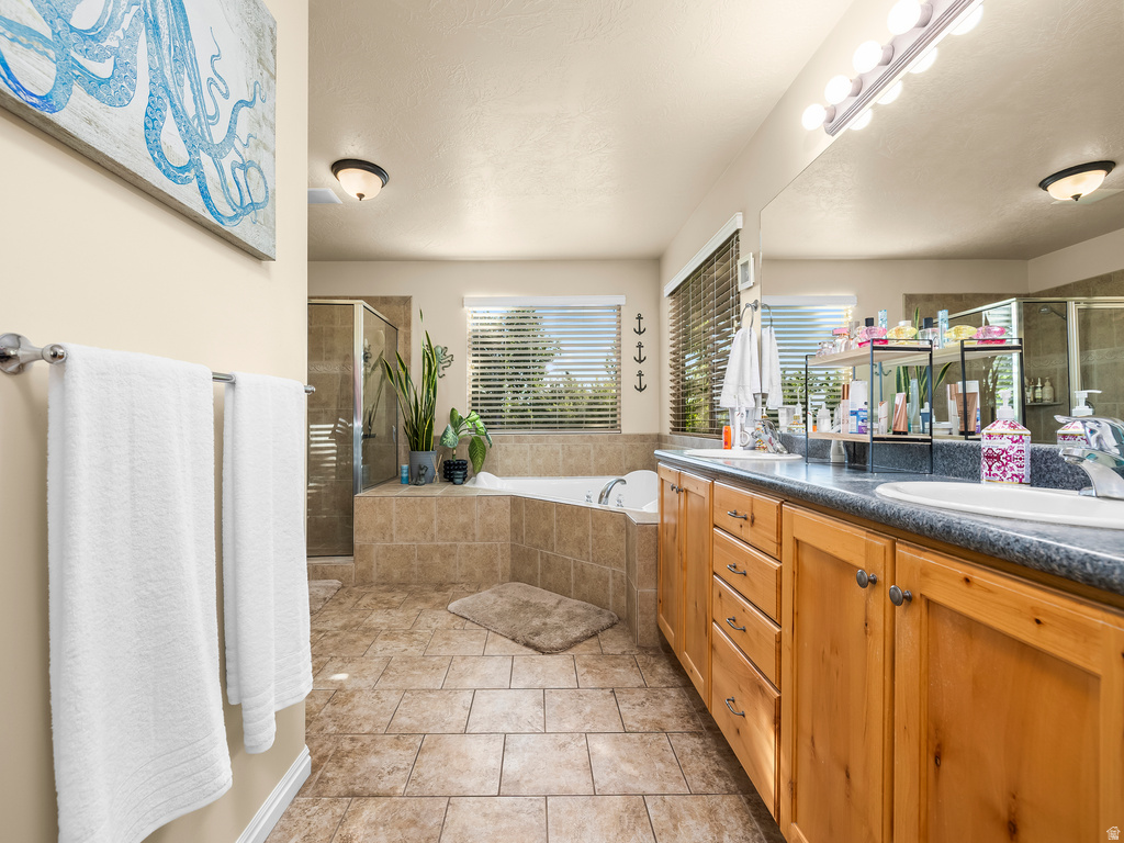 Bathroom featuring dual sink vanity with wood cabinetry, tiled flooring, built-in soaking tub, and a glass-enclosed shower