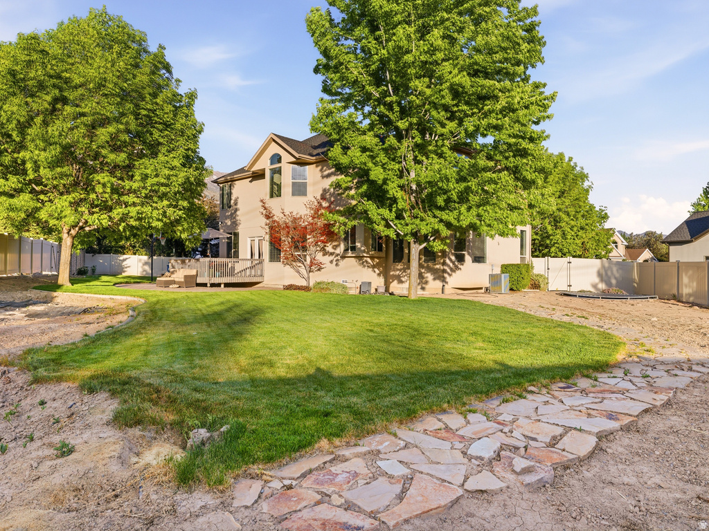 Rear exterior featuring a spacious lawn, mature trees, a multi-level wood deck, and a stone pathway