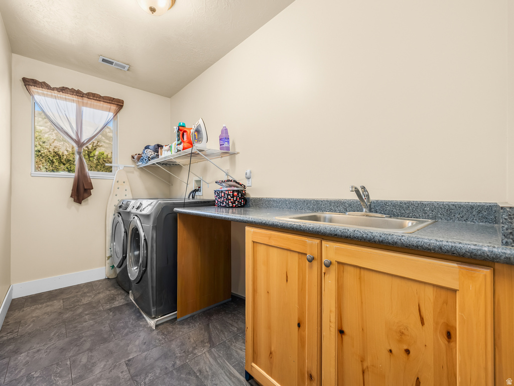 Dedicated laundry space featuring slate-style flooring, a window, built-in cabinetry, a utility sink, and a countertop