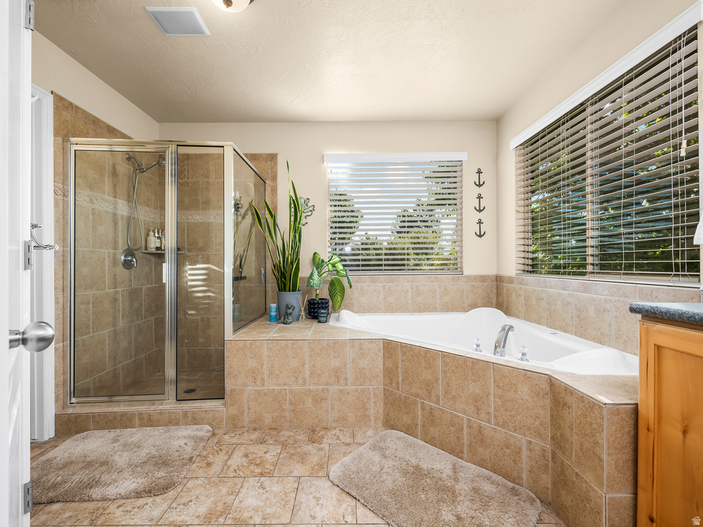 Tiled bathroom featuring a glass-enclosed shower, built-in corner soaking tub, and multiple windows with blinds