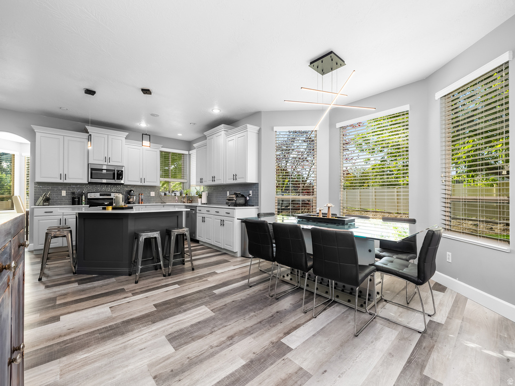 Contemporary kitchen and dining area featuring light-toned wood-finish flooring, a dark kitchen island, white cabinetry, and a textured tile backsplash