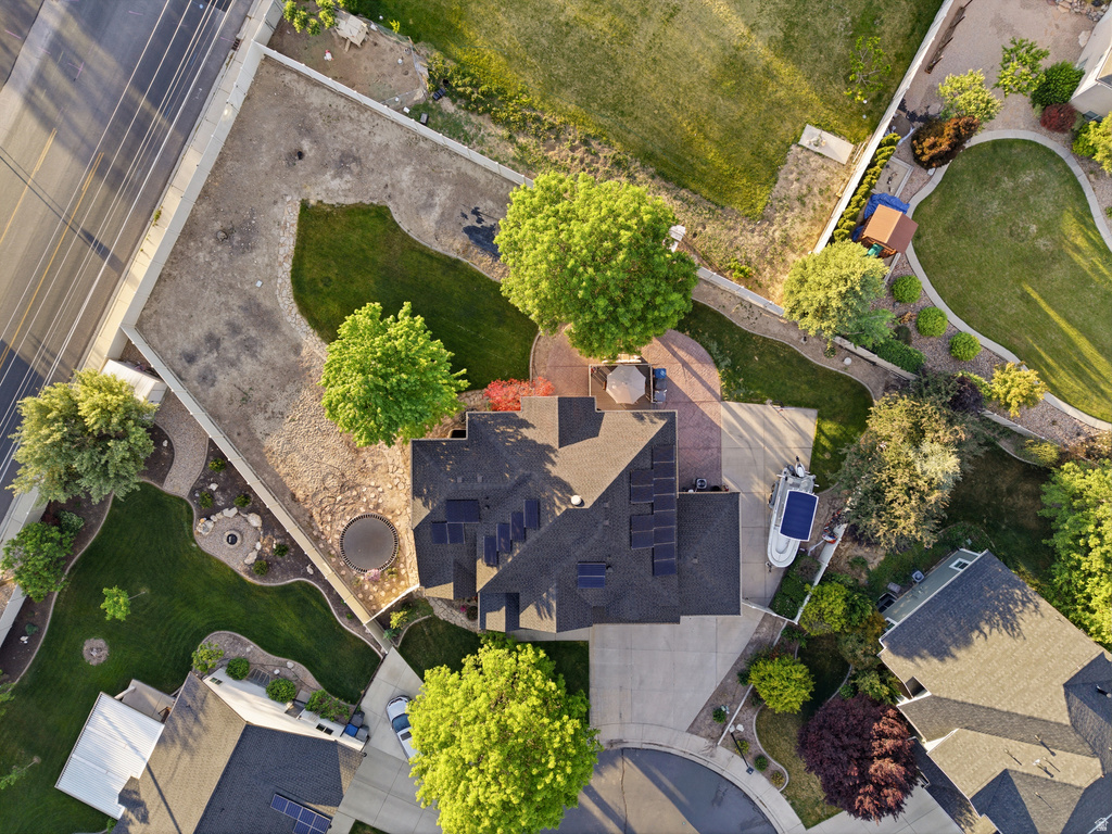 Expansive property featuring a dark shingle roof with solar panel installations, a large paved driveway, a circular fire pit area with stone seating, and mature landscaping with a mix of lawn and natural groundcover