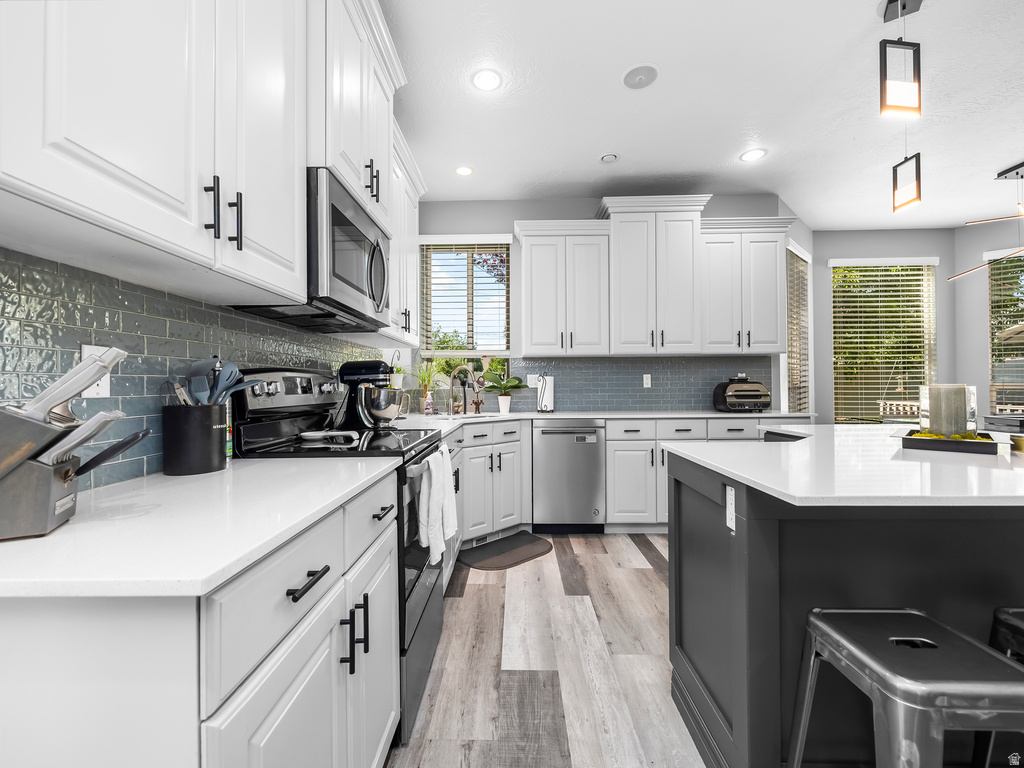Modern kitchen featuring white shaker cabinetry with matte black hardware, stainless steel appliances, a textured blue subway tile backsplash, light-toned wood-finish flooring, and a contrasting dark gray kitchen island with a white countertop