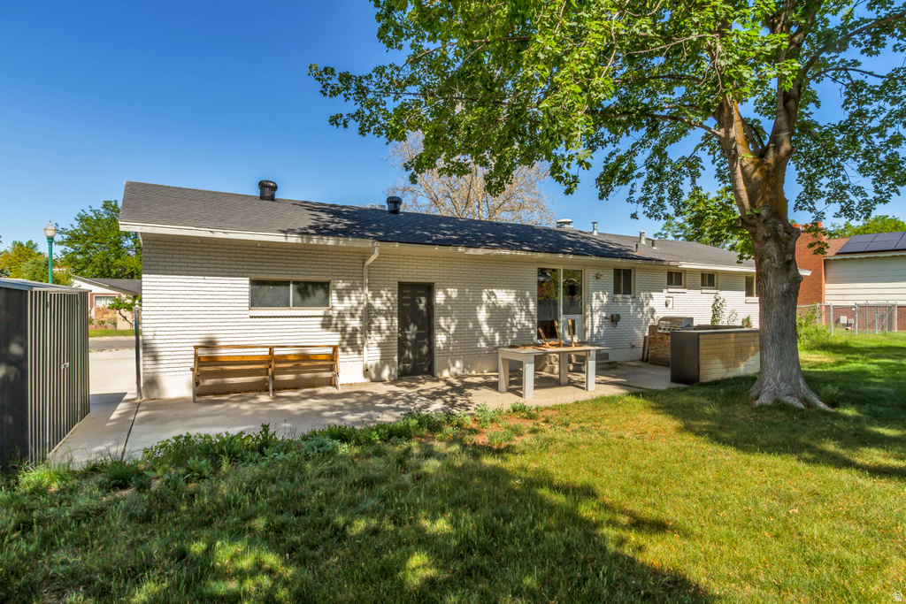 Rear exterior featuring a concrete patio, white brick facade, and a mature shade tree