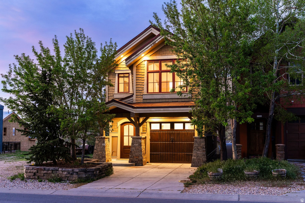 Craftsman-style facade featuring shingle siding, stone column accents, a covered entry, a wood-finish garage door, and architectural windows with red trim