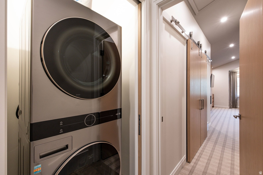 Stackable washer and dryer unit, light-toned wood-finish barn doors, recessed lighting, vaulted ceiling, and patterned carpet flooring