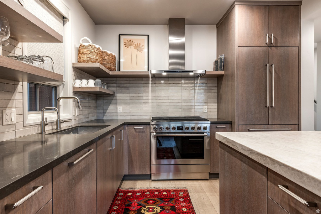 Gourmet kitchen featuring a stainless steel range with matching range hood, light wood-finish cabinetry, dark countertops, and a full-height tile backsplash