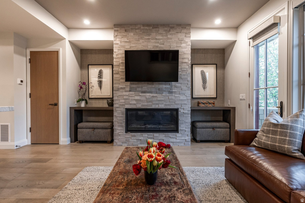 Living area featuring a stone-clad fireplace with an integrated linear firebox, wood-finish flooring, recessed lighting, and a glass-paneled exterior door