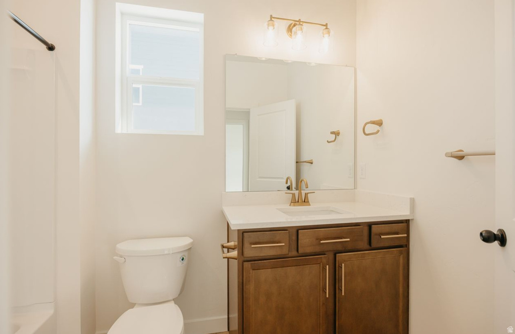 Bathroom featuring a wood-finish vanity with a light-toned countertop, an undermount sink, and a gold-finish faucet