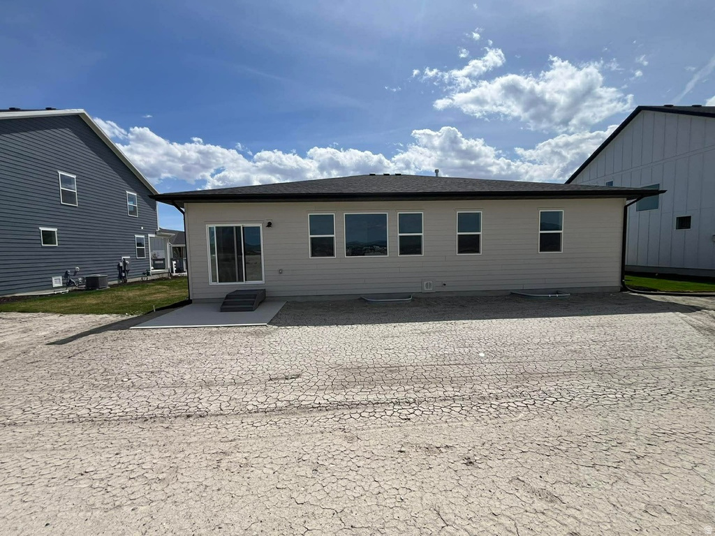 Rear exterior featuring beige siding, multiple windows, a sliding glass door, and a concrete patio