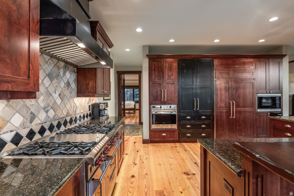 Gourmet kitchen featuring a stainless steel gas range with a professional-grade hood, granite countertops, and a full-height tile backsplash