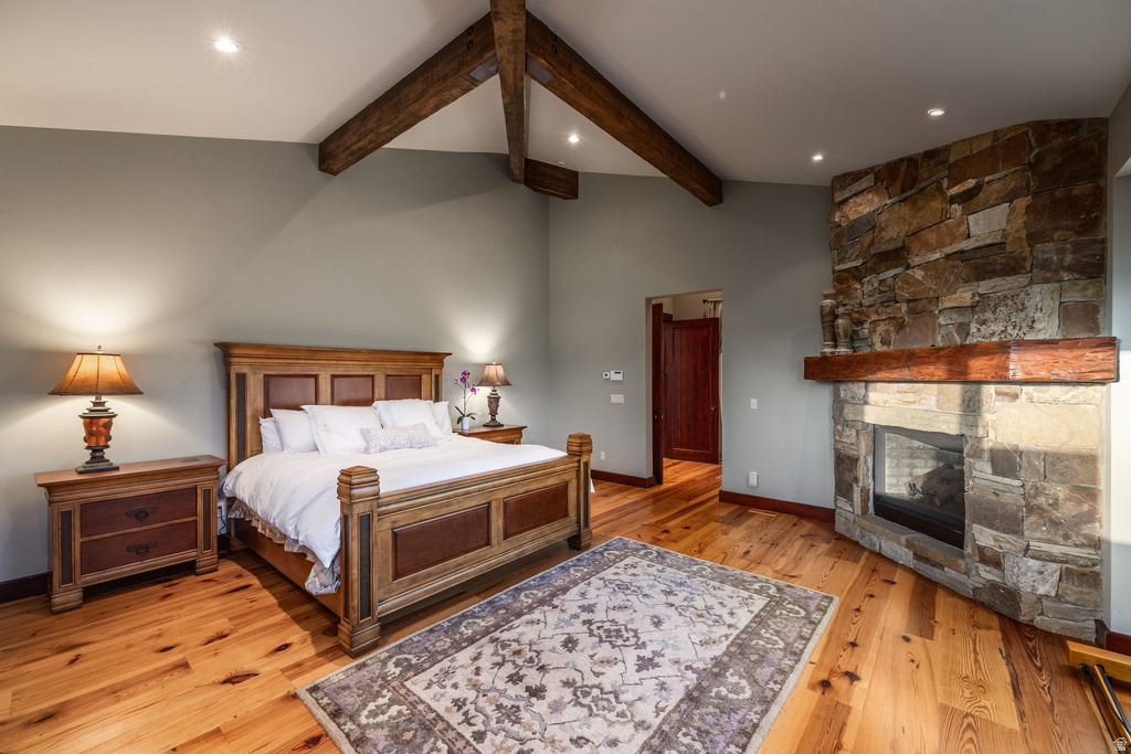 Spacious room featuring vaulted ceilings with exposed wood beams, a stone-clad fireplace with wood mantel, light wood-finish flooring, and recessed lighting