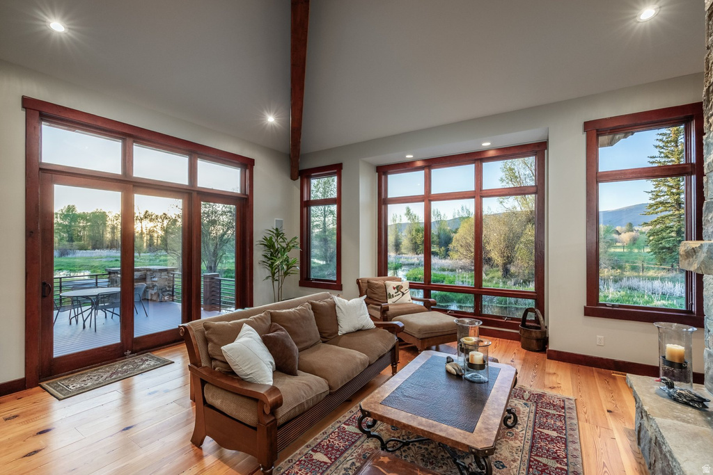Living area featuring wood-finish flooring, vaulted ceilings with exposed beams, recessed lighting, and large windows with dark wood trim