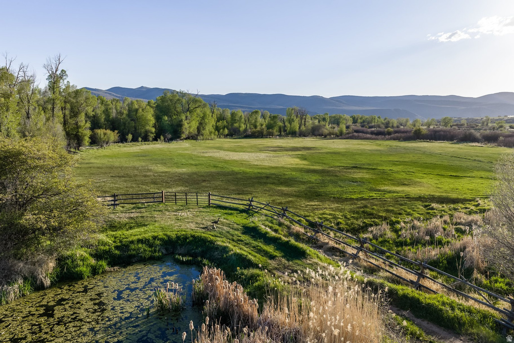 Expansive green pasture with a split rail fence, bordered by mature trees and a natural pond with reeds