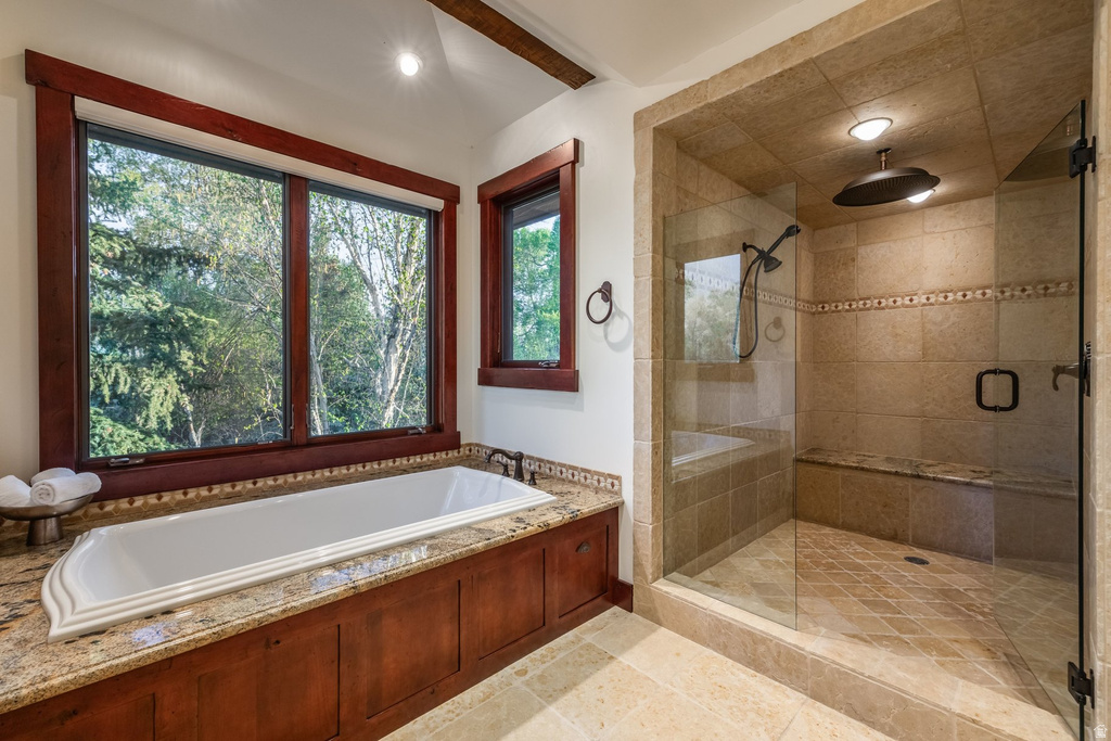 Spa-inspired bathroom featuring a built-in soaking tub with a stone-finish deck, a spacious walk-in shower with a built-in bench, and large windows with wood trim