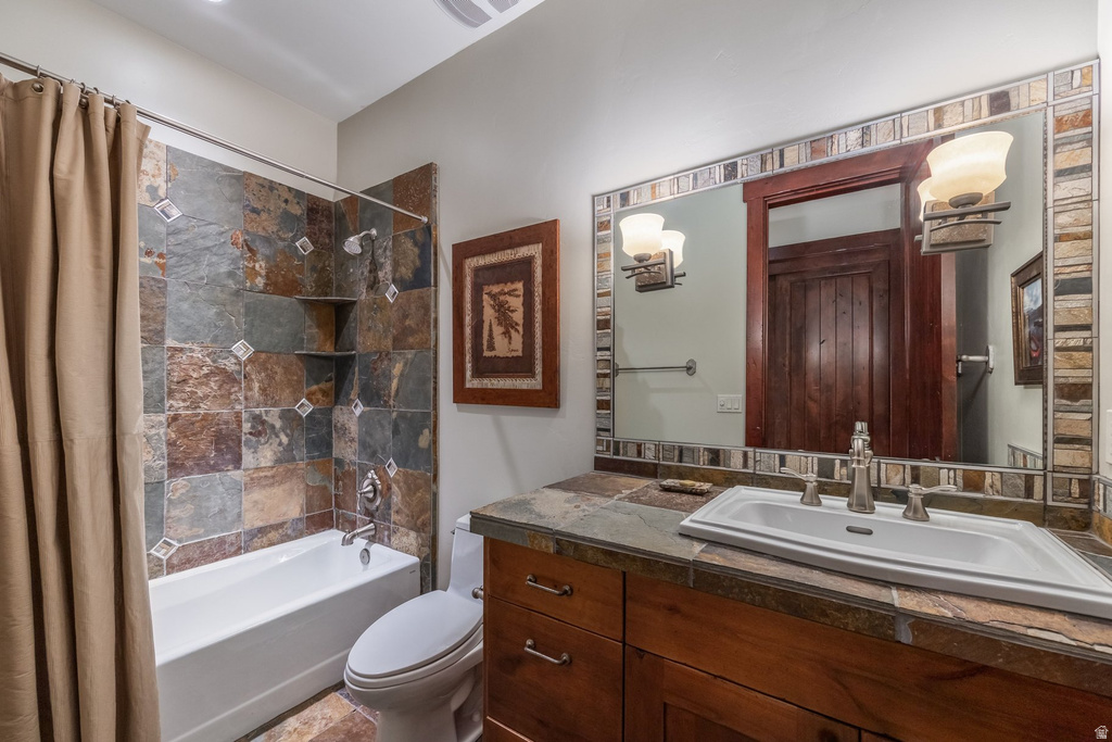 Bathroom featuring a tiled shower/tub combination, wood-finish vanity, stone countertop, and a vanity mirror with stone tile surround