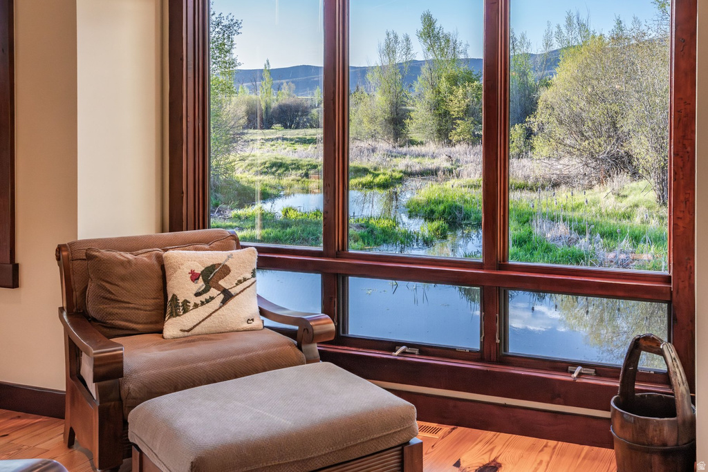 Expansive floor-to-ceiling windows with rich wood trim frame a natural landscape featuring a body of water and mature trees